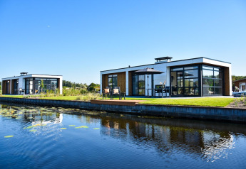 Moderne Villa Nautica-Lodges am Wasser mit großen Fenstern, Terrasse und schöner Aussicht bei Sonnenschein.