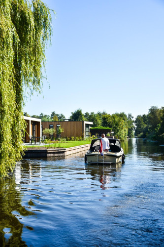 Eine Person fährt ein kleines Boot vor der Villa Nautica Lodge mit modernen Häusern und Bäumen am Ufer.
