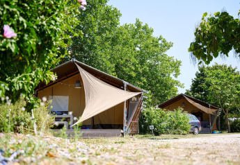 Safari tents at Villatent Nomad in Camping Les Bois du Bardelet, France, surrounded by lush green trees.