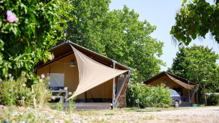 Safari tents at Villatent Nomad in Camping Les Bois du Bardelet, France, surrounded by lush green trees.