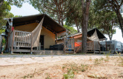 Tienda safari Villatent Nomad en Camping Village Cavallino, Italia, rodeada de pinos y terrazas de madera.