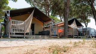 Tienda safari Villatent Nomad en Camping Village Cavallino, Italia, rodeada de pinos y terrazas de madera.