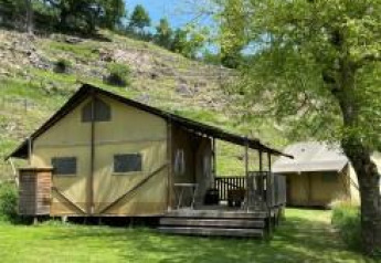 Et foto af et safaritelt med terrasse i naturskønt område, grøn græsplæne og træer i baggrunden.