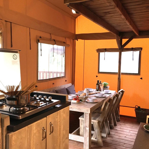Acogedora cocina y comedor de glamping en tienda de campaña con muebles de madera rústicos y mesa puesta.