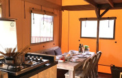 Acogedora cocina y comedor de glamping en tienda de campaña con muebles de madera rústicos y mesa puesta.