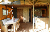 Indretning af luksustelt til glamping med træmøbler, spisebord, tekøkken og hyggelig atmosfære.