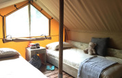 Interior de glamping acogedor con dos camas individuales, mesa de madera, oso de peluche y ventana grande.
