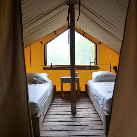 Interior de una tienda glamping con dos camas individuales sobre suelo de madera y una mesa entre ellas.