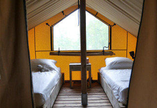 Interior de una tienda glamping con dos camas individuales sobre suelo de madera y una mesa entre ellas.
