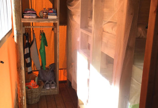 Alojamiento glamping con literas de madera, mosquitera y estante abierto con ropa y cesta en la tienda.