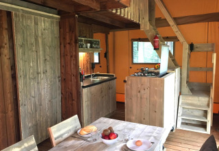 Acogedora cocina de glamping con muebles de madera, mesa de comedor, estufa y escaleras al altillo.