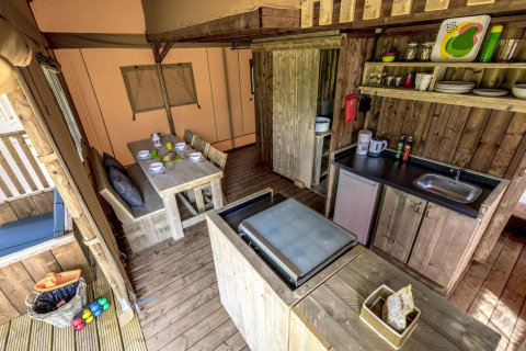 Cocina y comedor de glamping con muebles de madera, estanterías abiertas y vajilla completa.