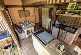Cocina y comedor de glamping con muebles de madera, estanterías abiertas y vajilla completa.