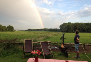Man looks at rainbow over green field at Feather Down De Lange Weide holiday park in Drenthe, Netherlands.