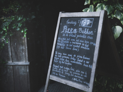 Udendørs tavle ved Feather Down De Lange Weide feriepark i Drenthe, Holland, med tekst om pizzabagning.