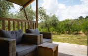 Udsigt fra safari-telt med komfortable kurvemøbler på Camping Pian Di Boccio, Italien, mod oliventræer.