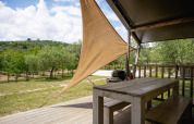 Blick von einem Safarizelt Villatent Nomad auf Camping Pian Di Boccio mit Holztisch, Bäumen und Grill.