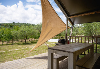 View from Villatent Nomad safari tent at Camping Pian Di Boccio, wooden table, shade, and surrounding trees.