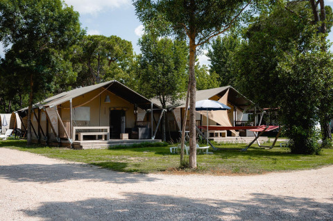 Tienda safari Villatent Nomad en Camping Punta Navaccia, Italia, rodeada de árboles y zonas de descanso al aire libre.