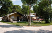 Tienda safari Villatent Nomad en Camping Punta Navaccia, Italia, rodeada de árboles y zonas de descanso al aire libre.