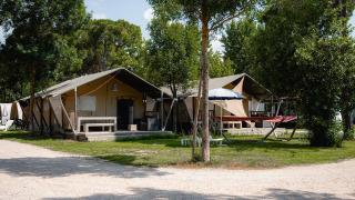 Safaritent Villatent Nomad op Camping Punta Navaccia in Italië, omgeven door bomen en zithoeken buiten.