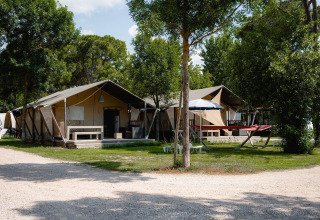 Tienda safari Villatent Nomad en Camping Punta Navaccia, Italia, rodeada de árboles y zonas de descanso al aire libre.