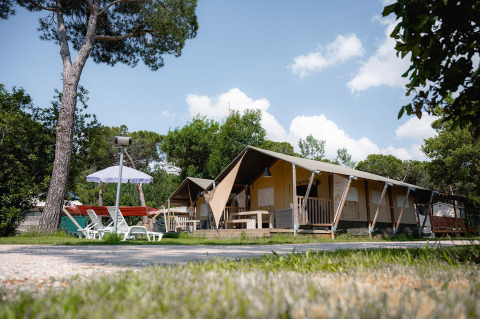 Tienda safari Villatent Nomad en el Camping Punta Navaccia en Italia con tumbonas y sombrilla afuera.