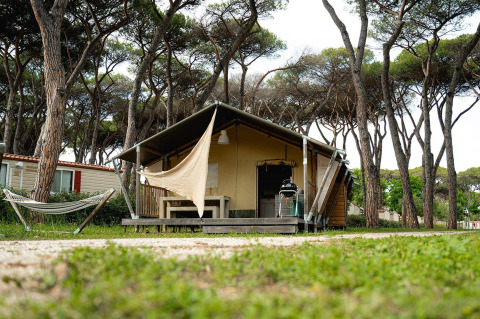 Tienda safari Villatent Nomad en Camping Roma Capitol en Italia, rodeada de pinos y una hamaca.