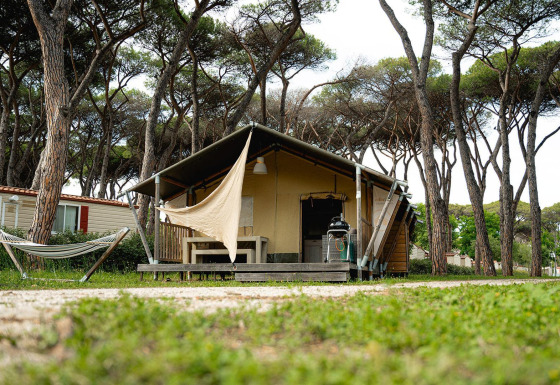 Safaritent Villatent Nomad op Camping Roma Capitol in Italië, omgeven door pijnbomen en een hangmat.