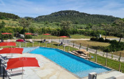 Piscina exterior con sombrillas rojas y tumbonas en Camping De l'Olivigne, Francia, rodeada de naturaleza.
