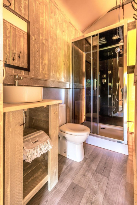 Baño dentro de la tienda Safari de Camping De l'Olivigne, Francia, con ducha, inodoro y acabados en madera.