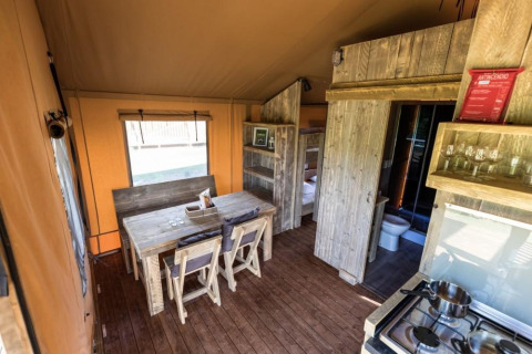 Interiør af en safaritelts med badeværelse på Camping De l'Olivigne, Frankrig, med rustikke træmøbler.