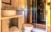 Bagno luminoso all'interno di una tenda safari, rivestito in legno, con doccia moderna, WC e lavabo.