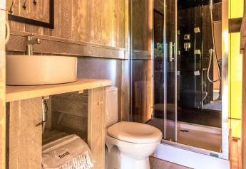 Baño luminoso en una tienda safari con paneles de madera, ducha moderna, inodoro y lavabo de cerámica.