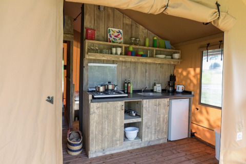 Pequeña cocina dentro de una tienda safari, con muebles de madera, estufa, fregadero y mini nevera.
