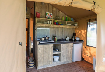 Pequeña cocina dentro de una tienda safari, con muebles de madera, estufa, fregadero y mini nevera.