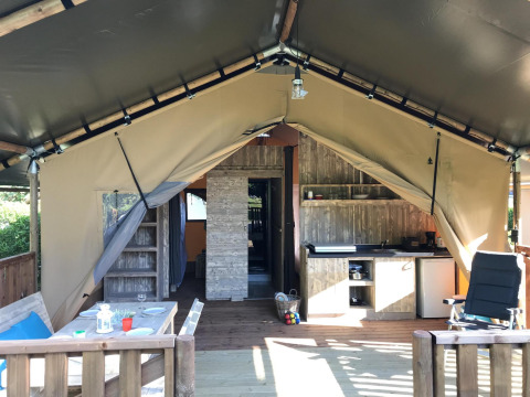Interior de una tienda safari de lujo con terraza de madera, cocina pequeña, mesa de comedor y asientos cómodos.