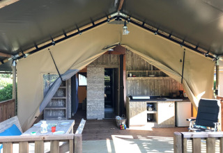 Interior de una tienda safari de lujo con terraza de madera, cocina pequeña, mesa de comedor y asientos cómodos.