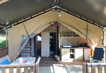 Interior de una tienda safari de lujo con terraza de madera, cocina pequeña, mesa de comedor y asientos cómodos.