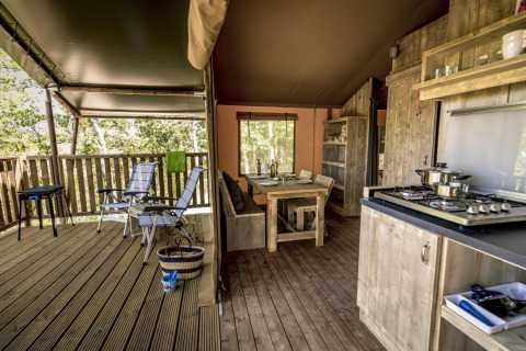 Tienda safari de lujo con muebles de madera, cocina abierta y terraza cubierta con sillas reclinables.