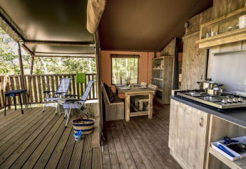 Tienda safari de lujo con muebles de madera, cocina abierta y terraza cubierta con sillas reclinables.