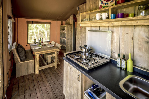 Interior de una tienda safari con cocina de madera, mesa de comedor rústica y estufa de gas moderna.