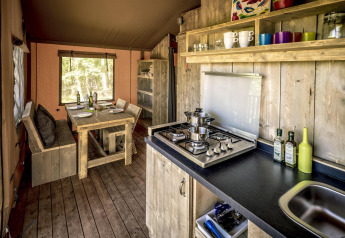 Interior de una tienda safari con cocina de madera, mesa de comedor rústica y estufa de gas moderna.