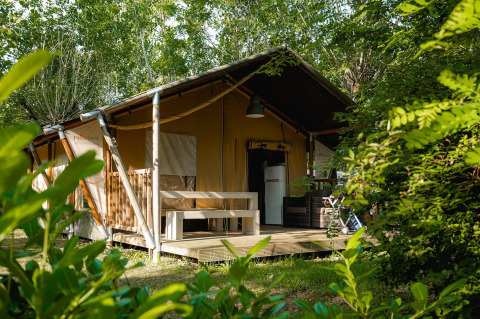 Tienda safari Villatent Nomad en Camping La Chiocciola, Italia, rodeada de vegetación y árboles verdes.