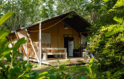 Tienda safari Villatent Nomad en Camping La Chiocciola, Italia, rodeada de vegetación y árboles verdes.