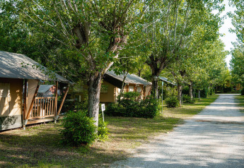 Tienda safari Villatent Nomad en Camping La Chiocciola, Italia, con árboles y senderos tranquilos alrededor.