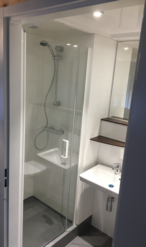 Baño compacto en una tienda safari en Holiday park Eigen Wijze con ducha, lavabo, estantes y espejo.
