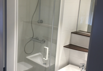 Baño compacto en una tienda safari en Holiday park Eigen Wijze con ducha, lavabo, estantes y espejo.