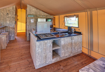 Indvendigt af et safaritelts køkkenområde med trægulve, gasblus og vinduer på Holiday park Eigen Wijze.