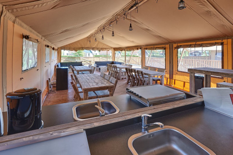Interior view of a safari group tent at Holiday Park Eigen Wijze, featuring dining tables and kitchen.